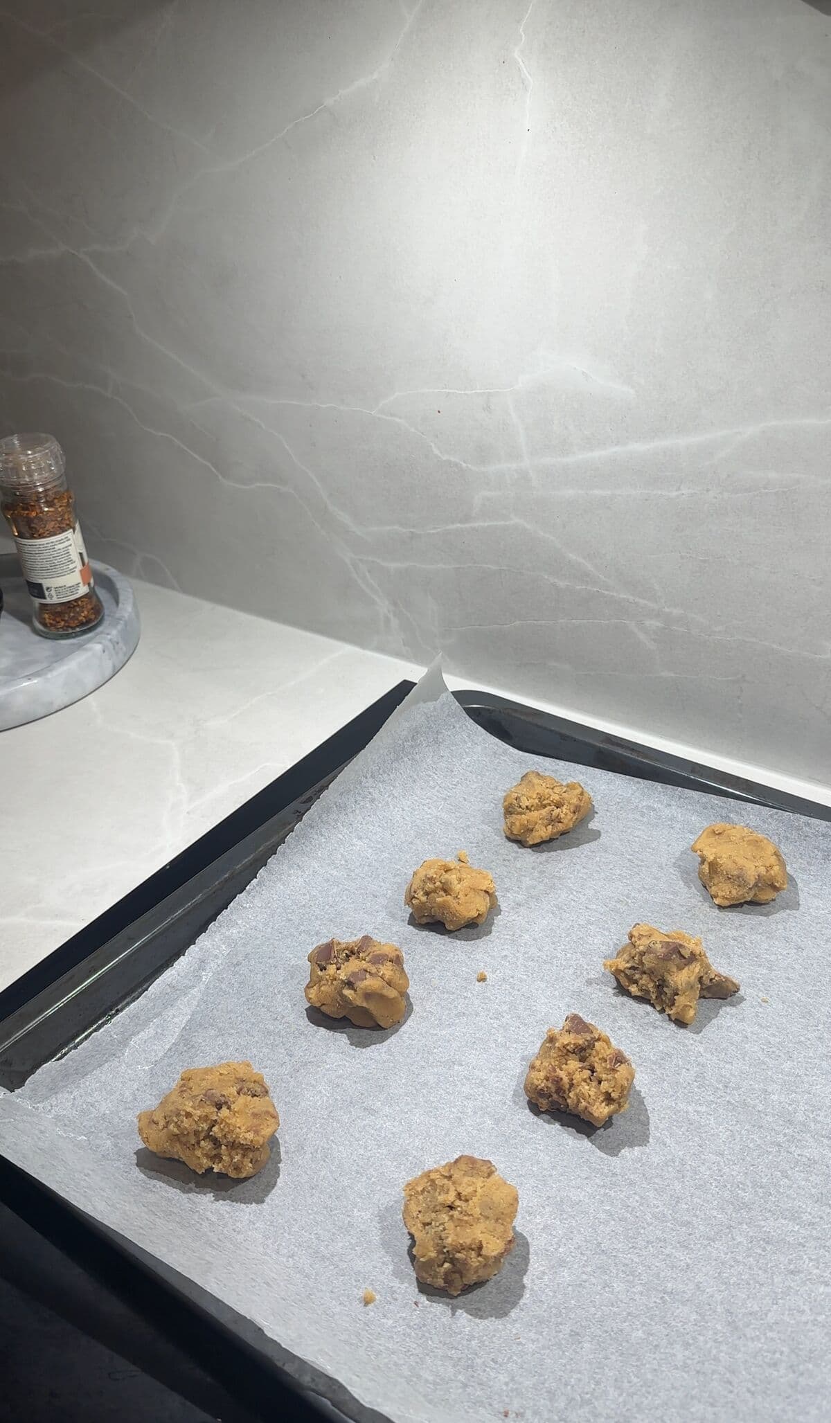 Skiver av cookie dough fordelt på et stekebrett, klare for ovnen
